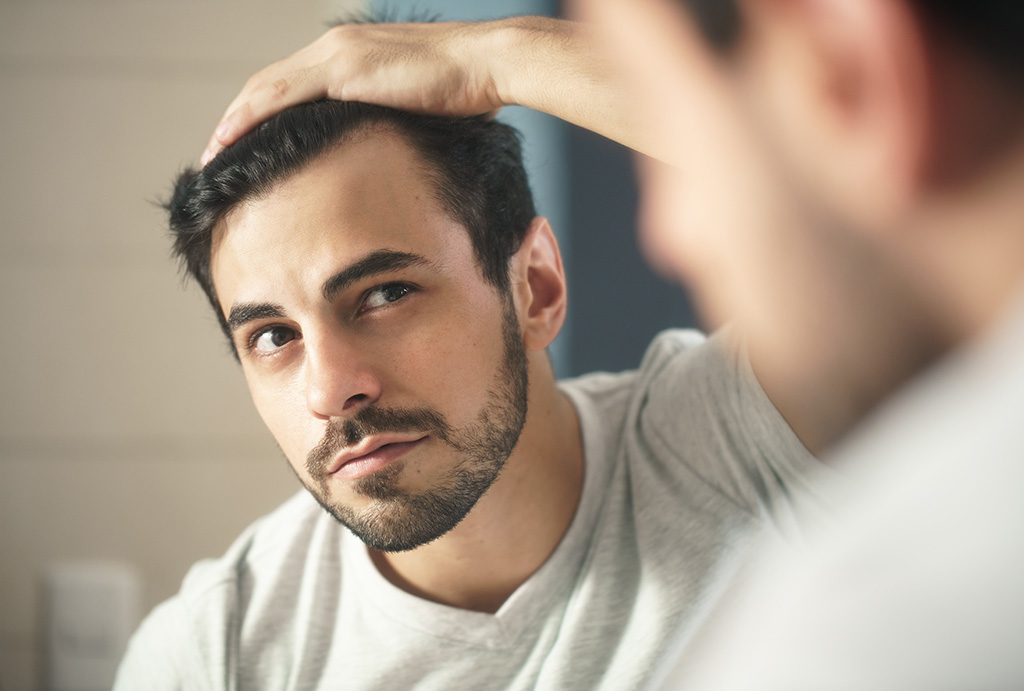 man looking at hair in mirror